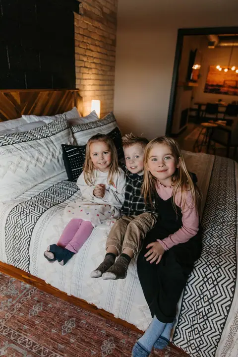 Three young kids sitting together on a bed in a Brix condo bedroom