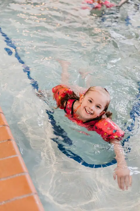 A smiling girl in a swim vest swimming in the indoor pool at the Waterfront Plaza building in Canal Park