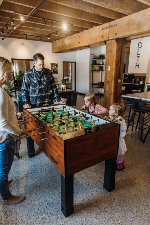 Family playing foosball in a Brix condo loft with exposed beams in Canal Park