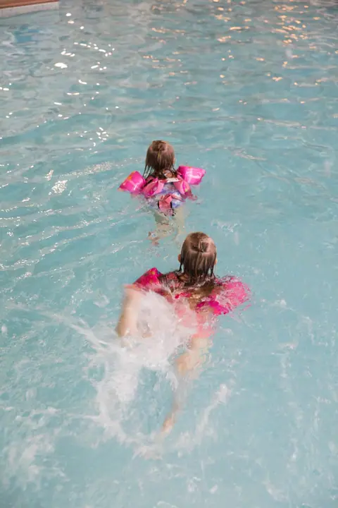 Two kids in pink swim vests swimming in the indoor pool at the Waterfront Plaza building in Canal Park